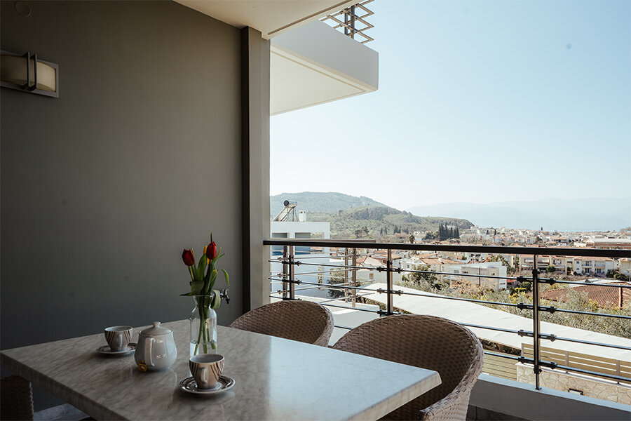 A vacation apartment balcony in Nafplio, Greece with with chairs, a table, and a vase of flowers.